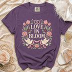 Purple t-shirt with "Love In Bloom" text, wedding rings, doves, and floral design.