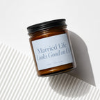 Amber glass candle with black lid and blue label reading "Married Life Looks Good on Us".
