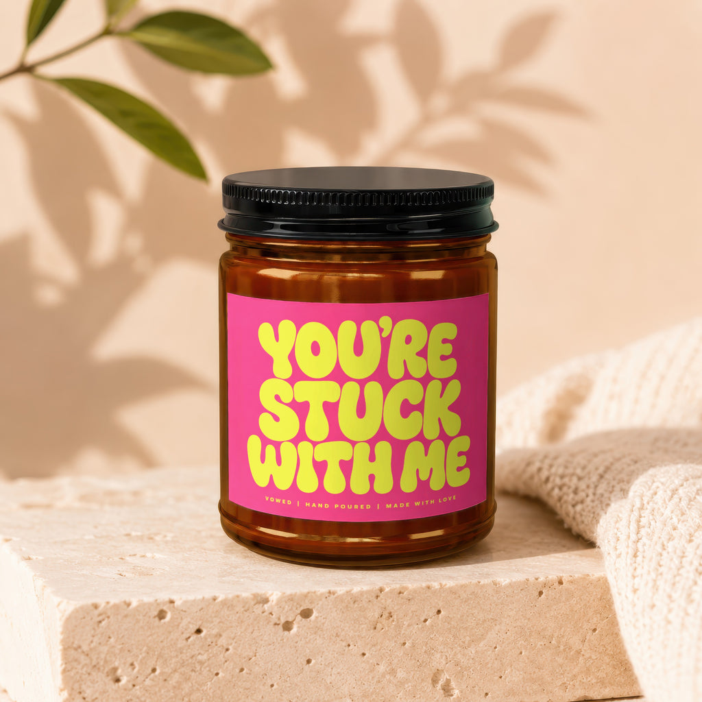 Glass jar candle with a neon pink label that says "YOU'RE STUCK WITH ME".