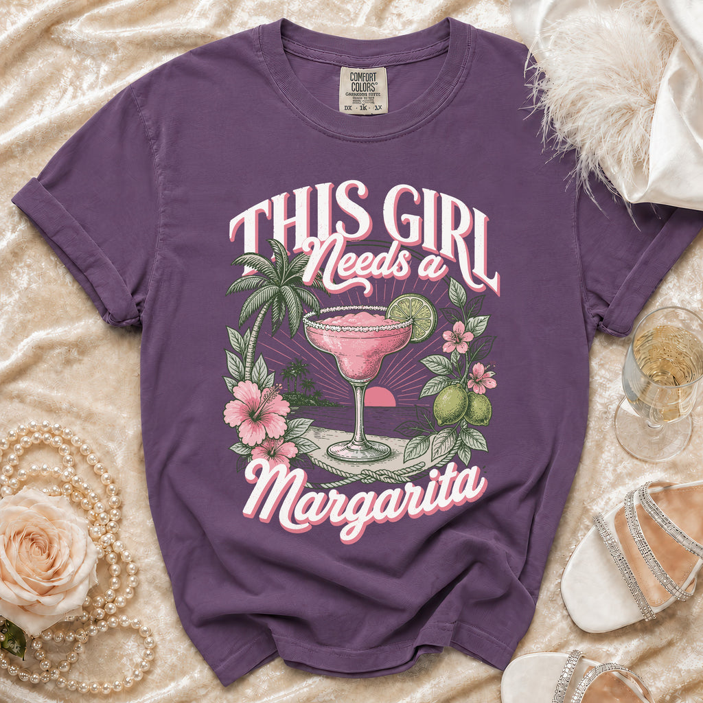 Purple t-shirt graphic with text "This Girl Needs a Margarita" and tropical drink.