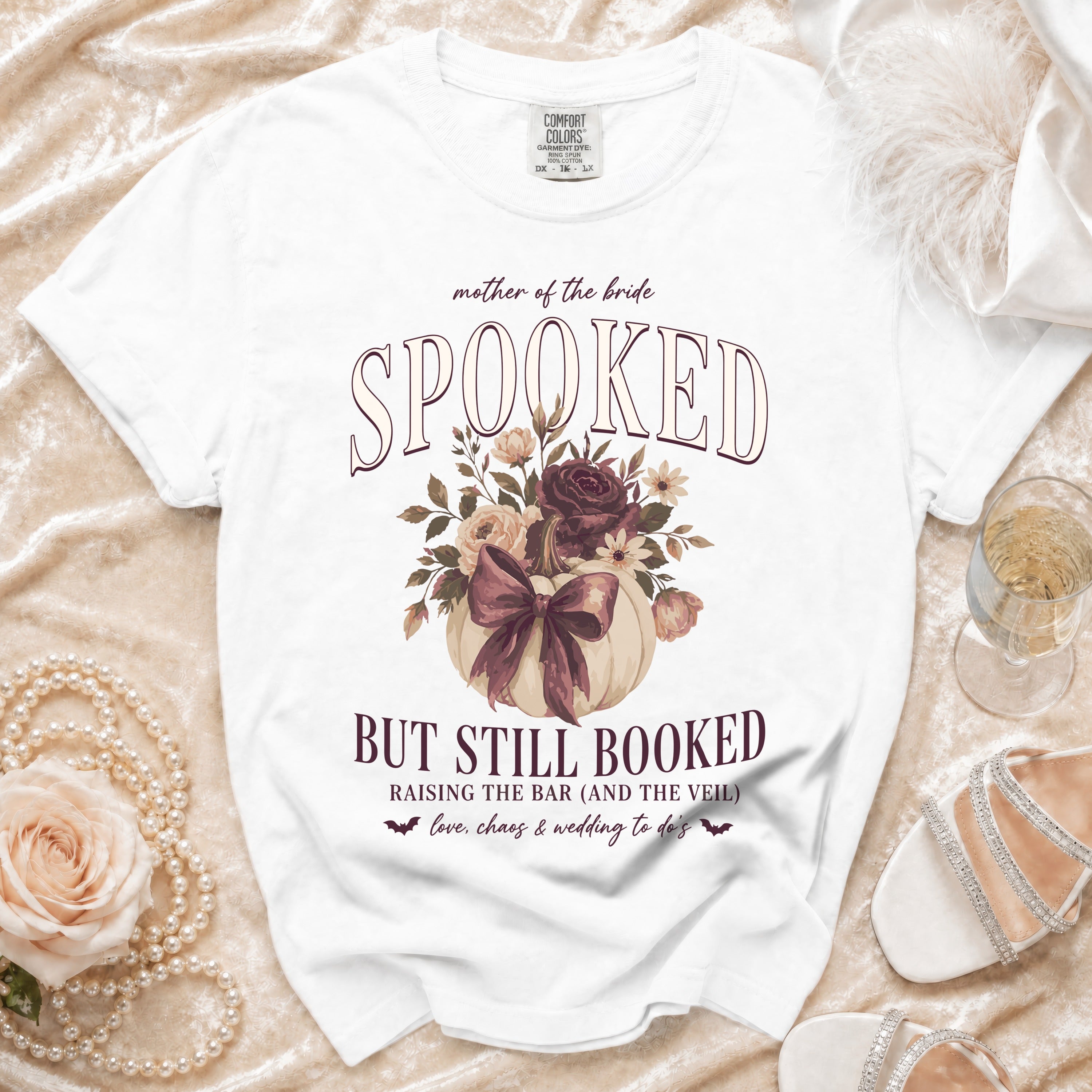 White t-shirt with "mother of the bride SPOOKED BUT STILL BOOKED" Halloween wedding graphic.