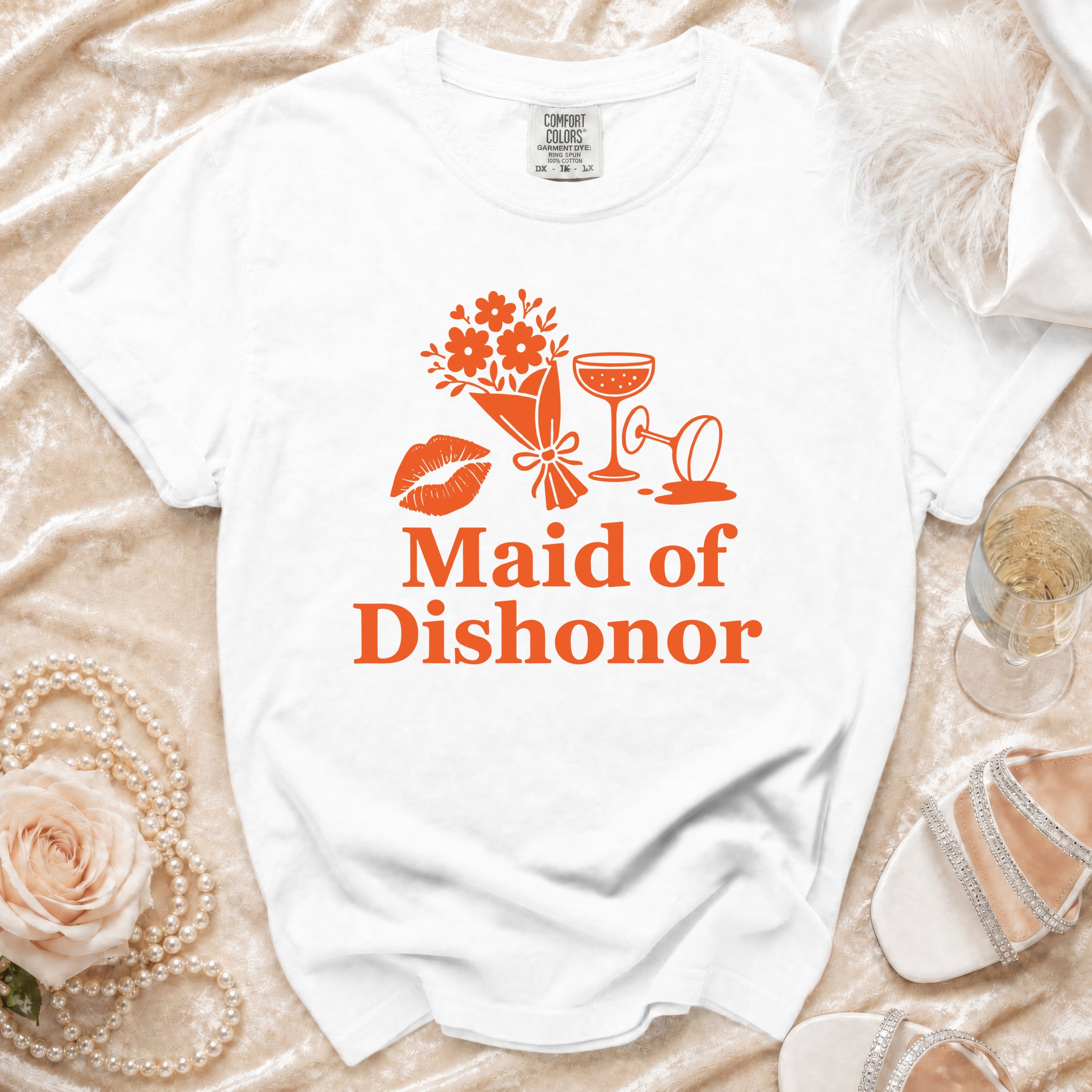 White t-shirt with orange graphic: "Maid of Dishonor," lipstick, flowers, and cocktail glasses.