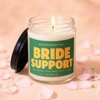 Candle with label reading "DEPARTMENT OF: BRIDE SUPPORT OPEN TWENTY-FOUR HOURS. STAFF OF ONE. VOWED."