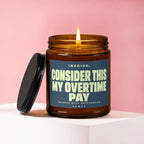 Candle in amber glass jar with lid off, lit wick, and label reading "INVOICE: CONSIDER THIS MY OVERTIME PAY".