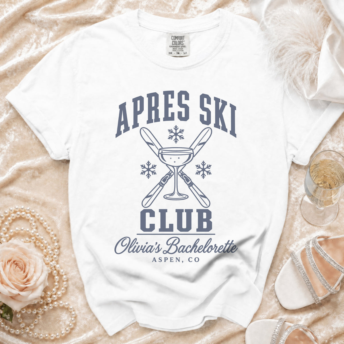 White t-shirt with Apres Ski Club bachelorette text and a martini glass design on a velvet background.