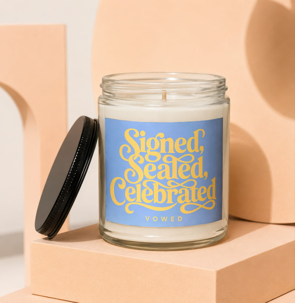 Glass candle with "Signed, Sealed, Celebrated VOWED" text on a blue label.