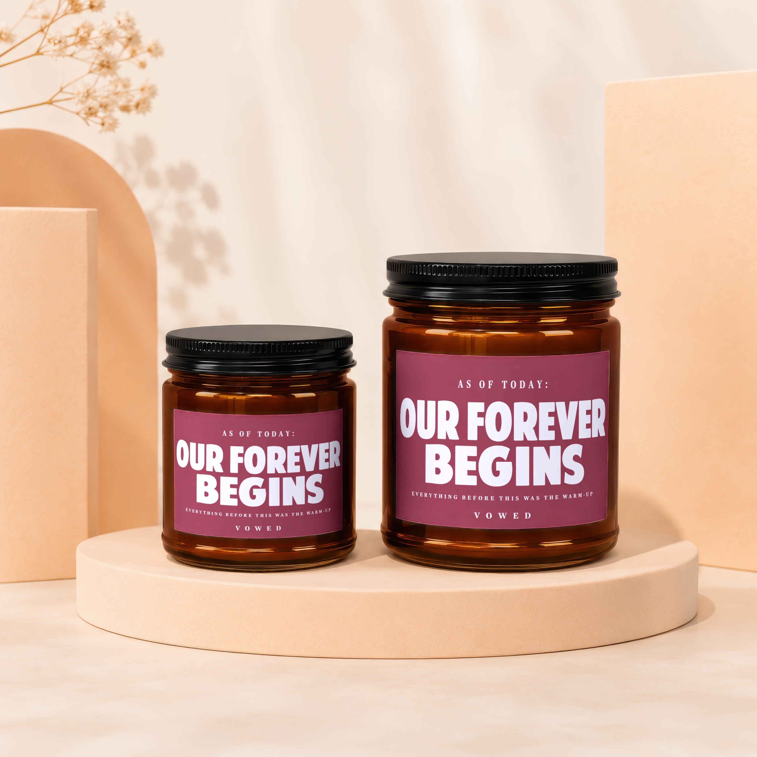 Two amber glass candles with maroon labels reading "Our Forever Begins".