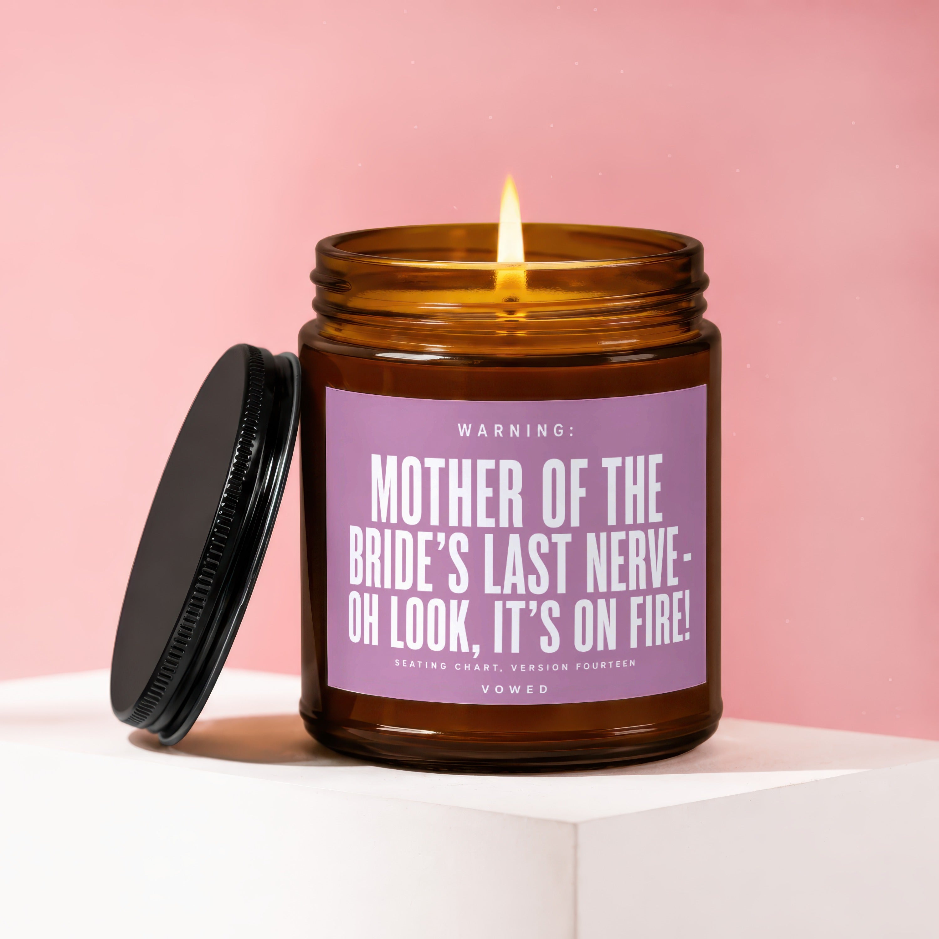 Amber jar candle with lit wick, reads "Mother of the Bride's Last Nerve - Oh Look, It's On Fire!".
