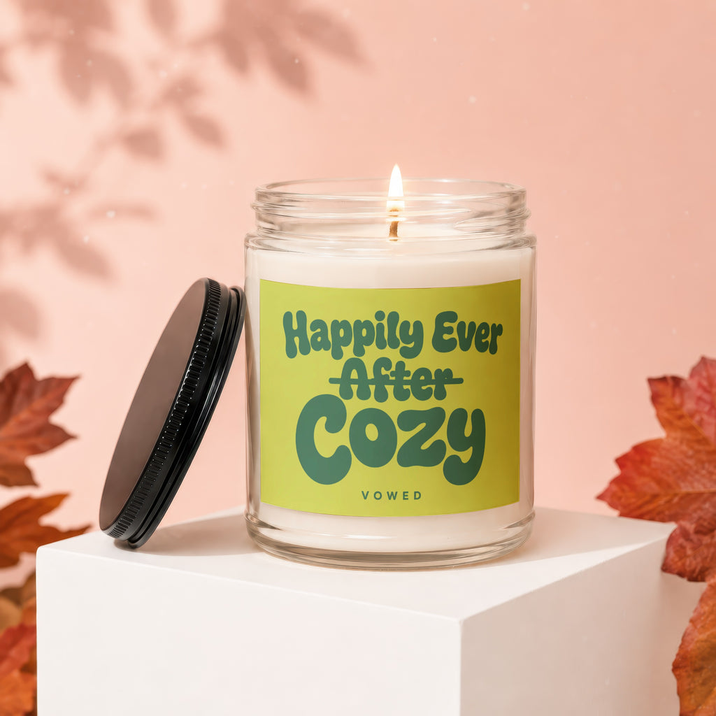 Glass candle with lid titled "Happily Ever After Cozy Vowed" surrounded by autumn leaves.