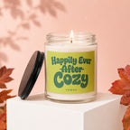 Glass candle with lid titled "Happily Ever After Cozy Vowed" surrounded by autumn leaves.