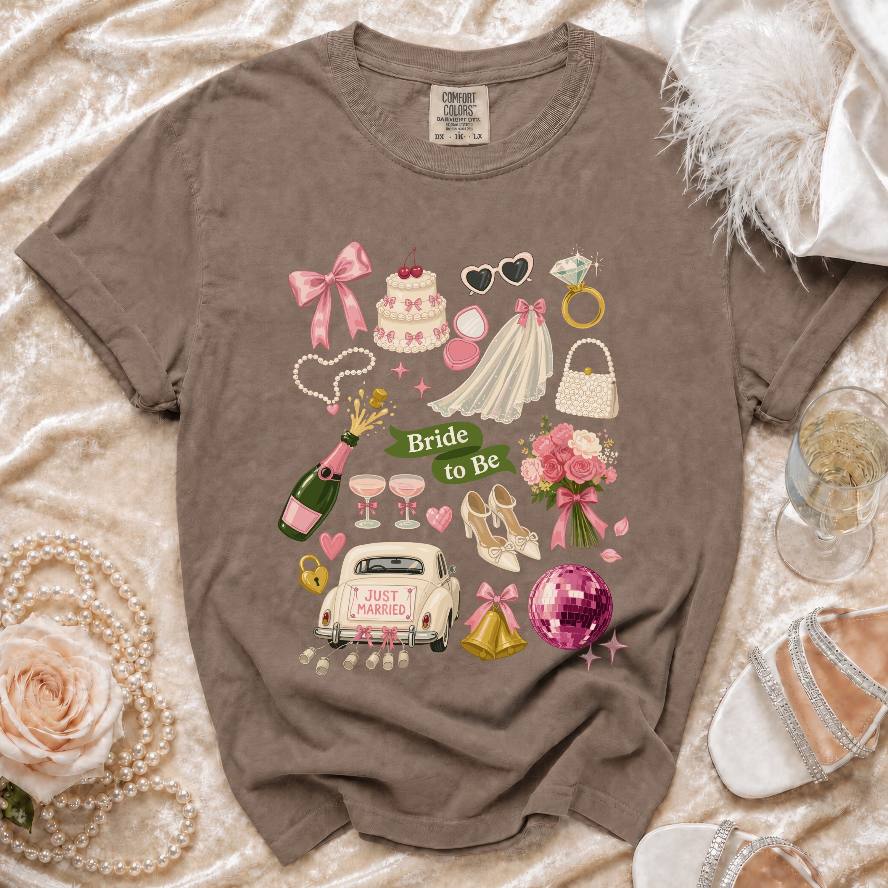 T-shirt with "Bride to Be" graphic featuring wedding items: car, cake, veil, ring, and champagne.