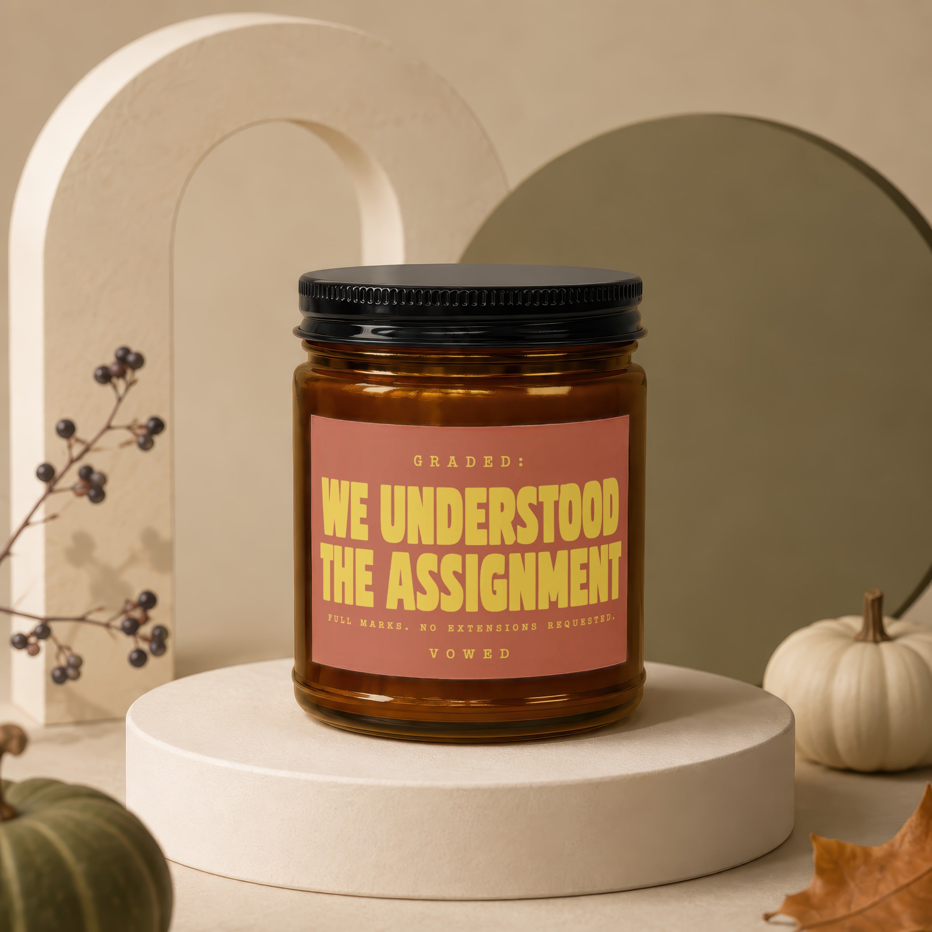 Amber candle with black lid, label reads "GRADED: WE UNDERSTOOD THE ASSIGNMENT."