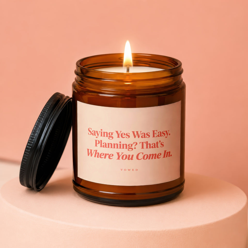 Amber jar candle with lit wick, featuring text "Saying Yes Was Easy. Planning? That's Where You Come In."