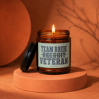 Amber glass candle with lit wick and black lid, reads "Team Bride Recruit Veteran Vowed".