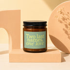 Amber candle with black lid and green label reading "Two last names, one love VOWED".
