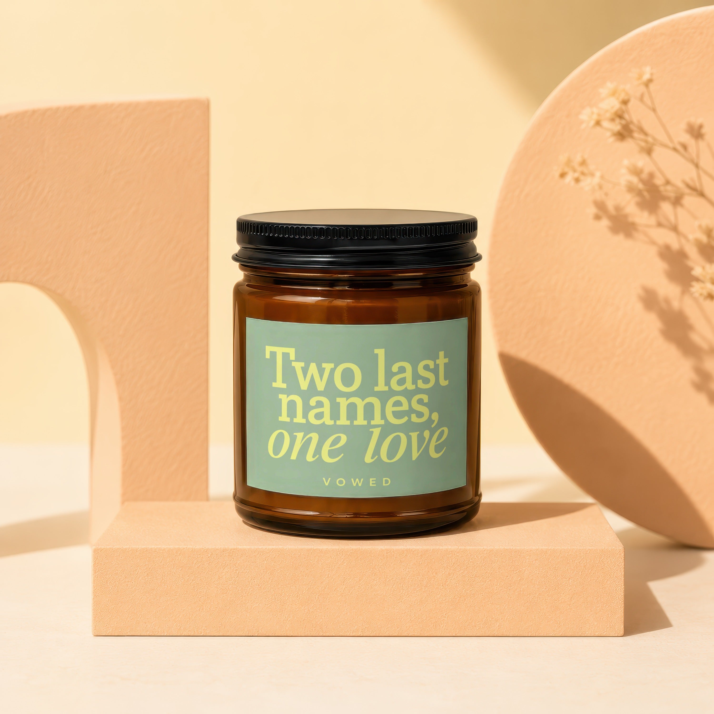 Amber candle with black lid and green label reading "Two last names, one love VOWED".