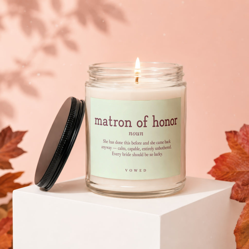 Lit candle in a glass jar labeled "matron of honor" with descriptive text.