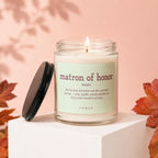 Lit candle in a glass jar labeled "matron of honor" with descriptive text.