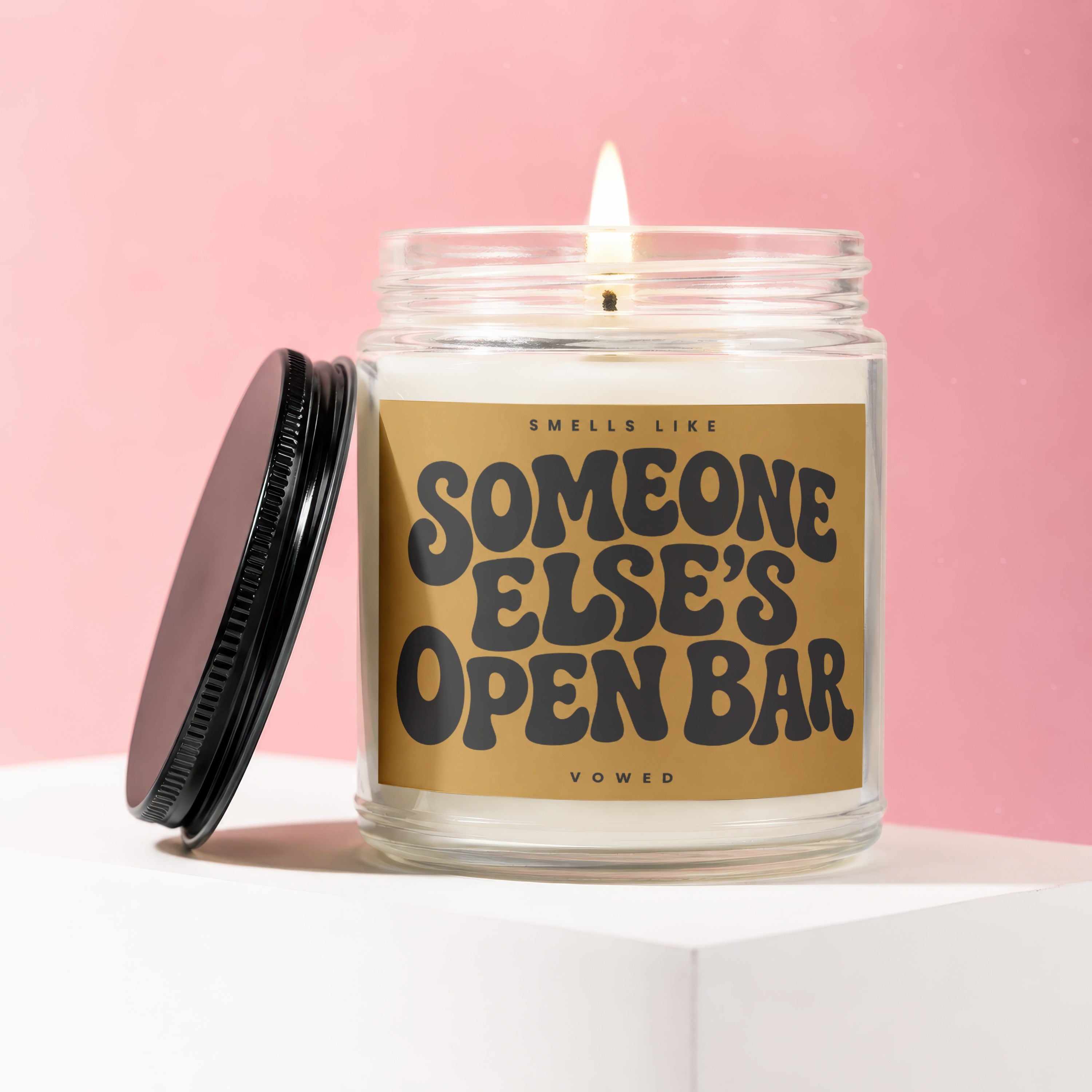 Lit candle in a jar with a black lid, reading "Smells Like Someone Else's Open Bar."