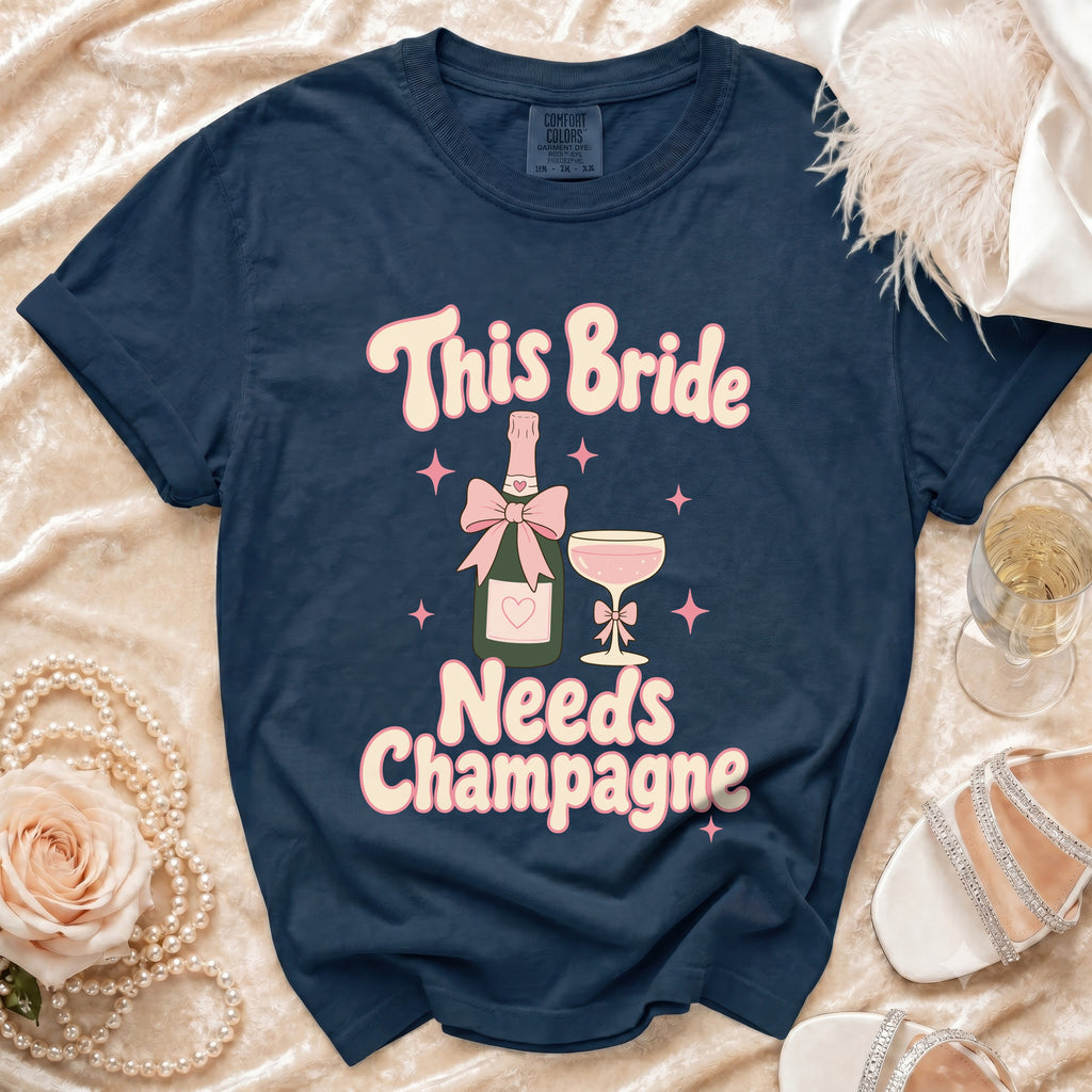 Navy t-shirt with "This Bride Needs Champagne" text, champagne bottle, and glass.
