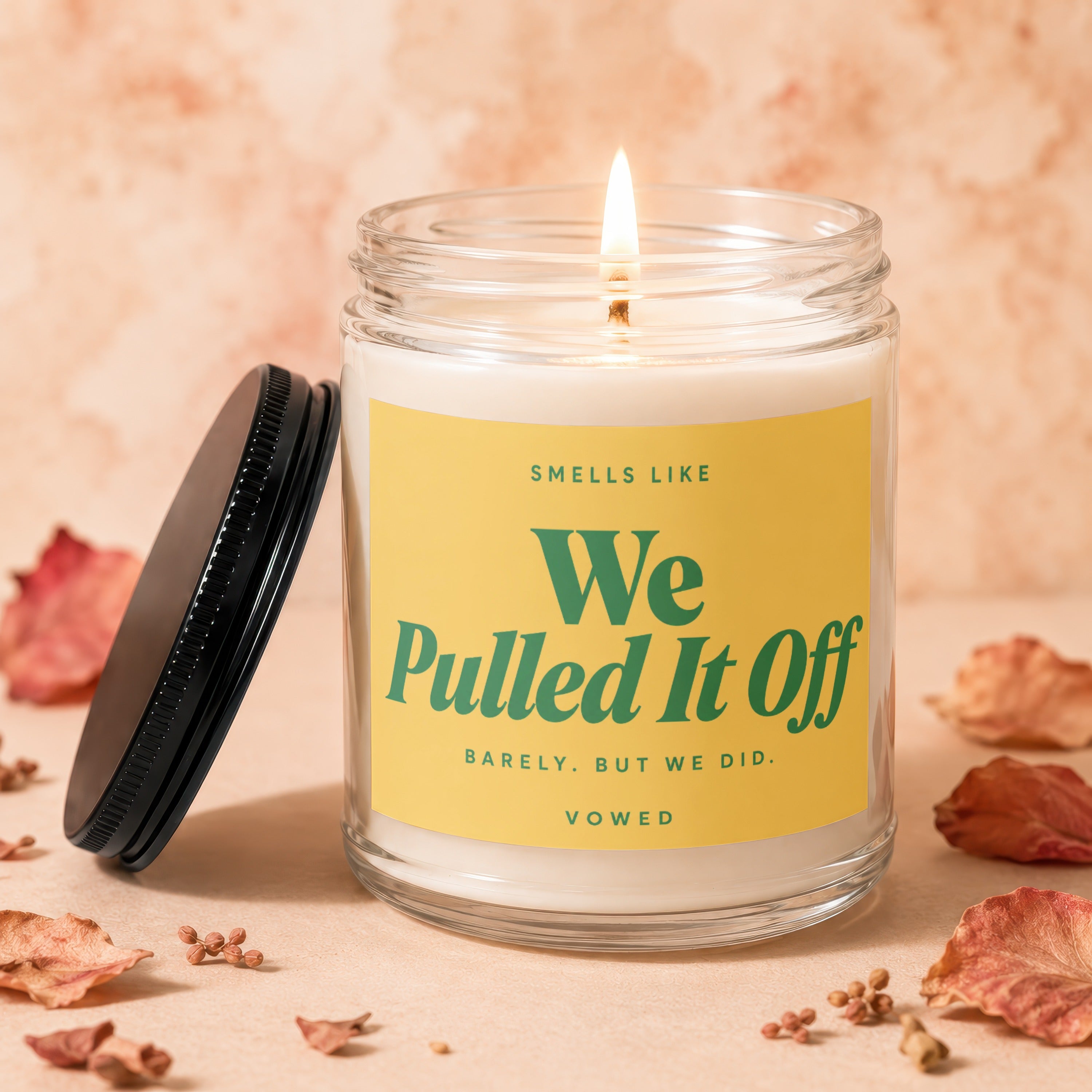 Glass candle with lit wick and yellow label reading "We Pulled It Off".
