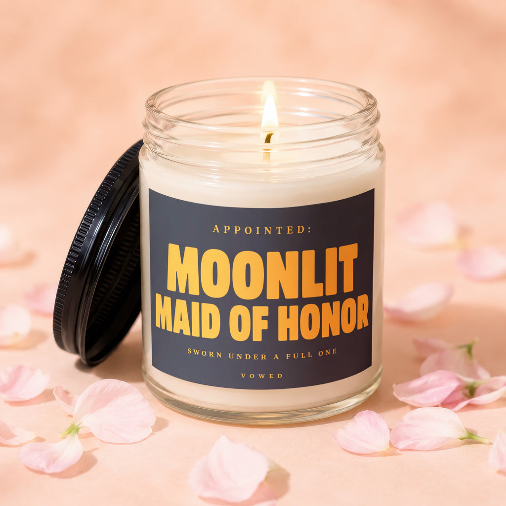 Lit candle with "MOONLIT MAID OF HONOR" text on the label, surrounded by pink petals.