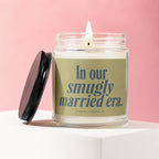 Glass candle with lit wick, a black lid, and text "In our smugly married era."