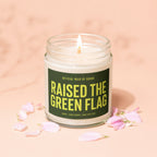 Candle with "Raised the Green Flag" text in a glass jar with pink petal accents.