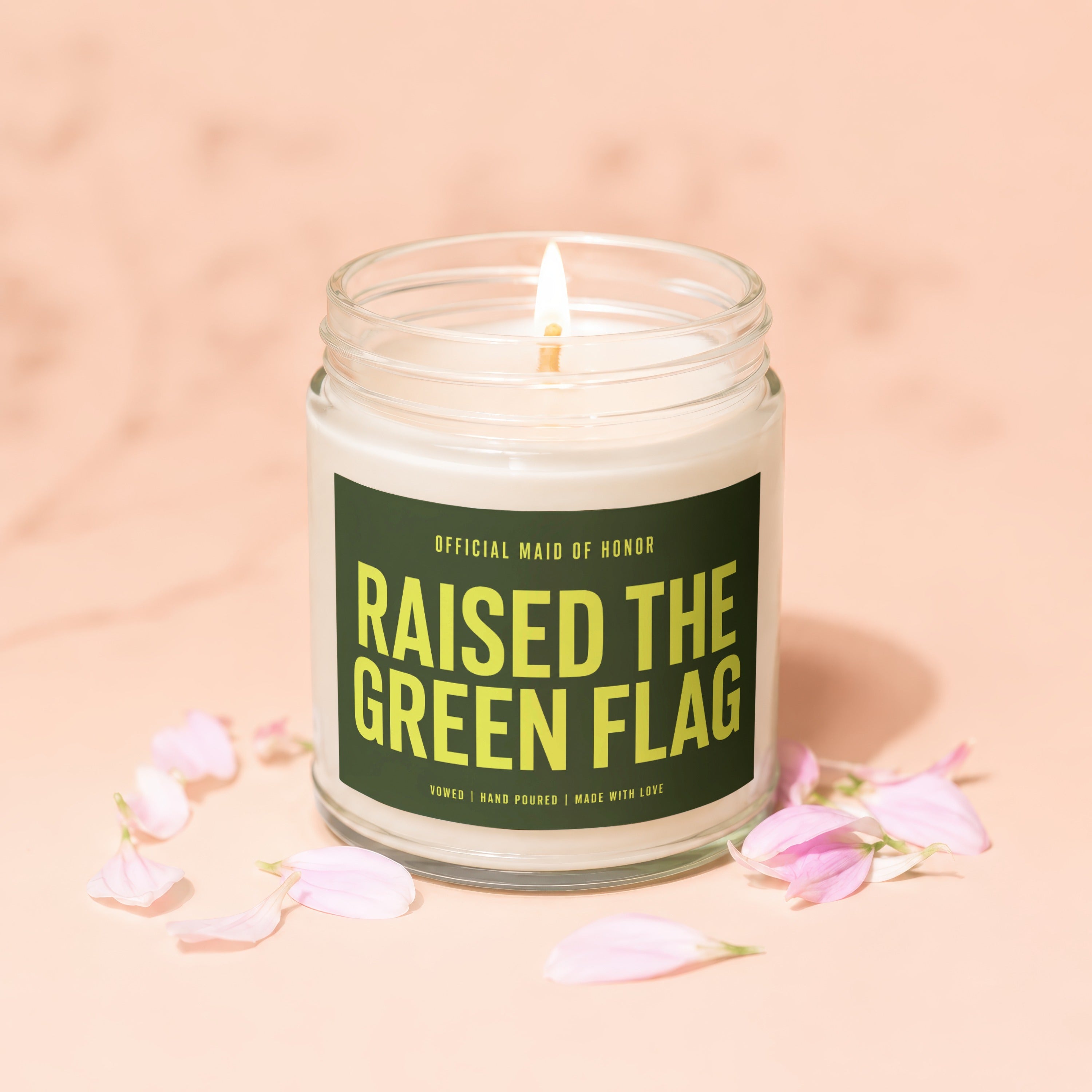 Candle with "Raised the Green Flag" text in a glass jar with pink petal accents.