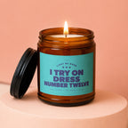 Amber glass candle with teal label reading "Light me when I try on dress number twelve."