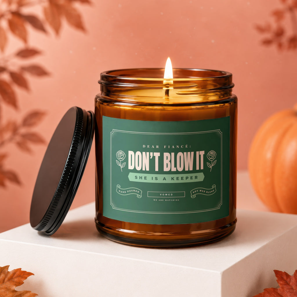 Amber jar candle with lit wick and green label reading "Don't Blow It She is a Keeper".