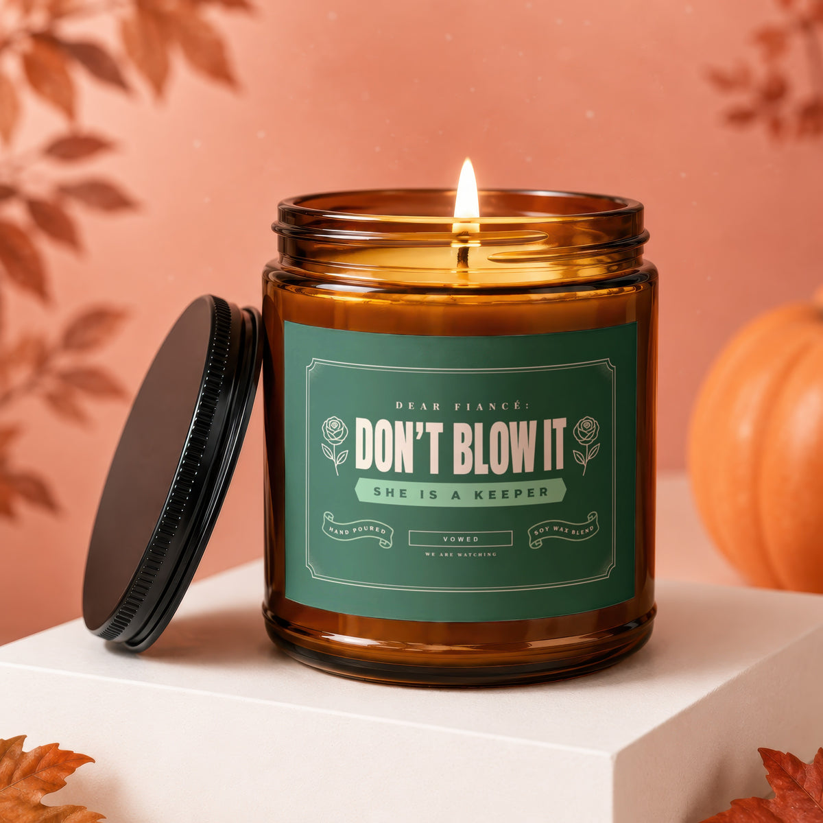 Amber jar candle with lit wick and green label reading "Don't Blow It She is a Keeper".