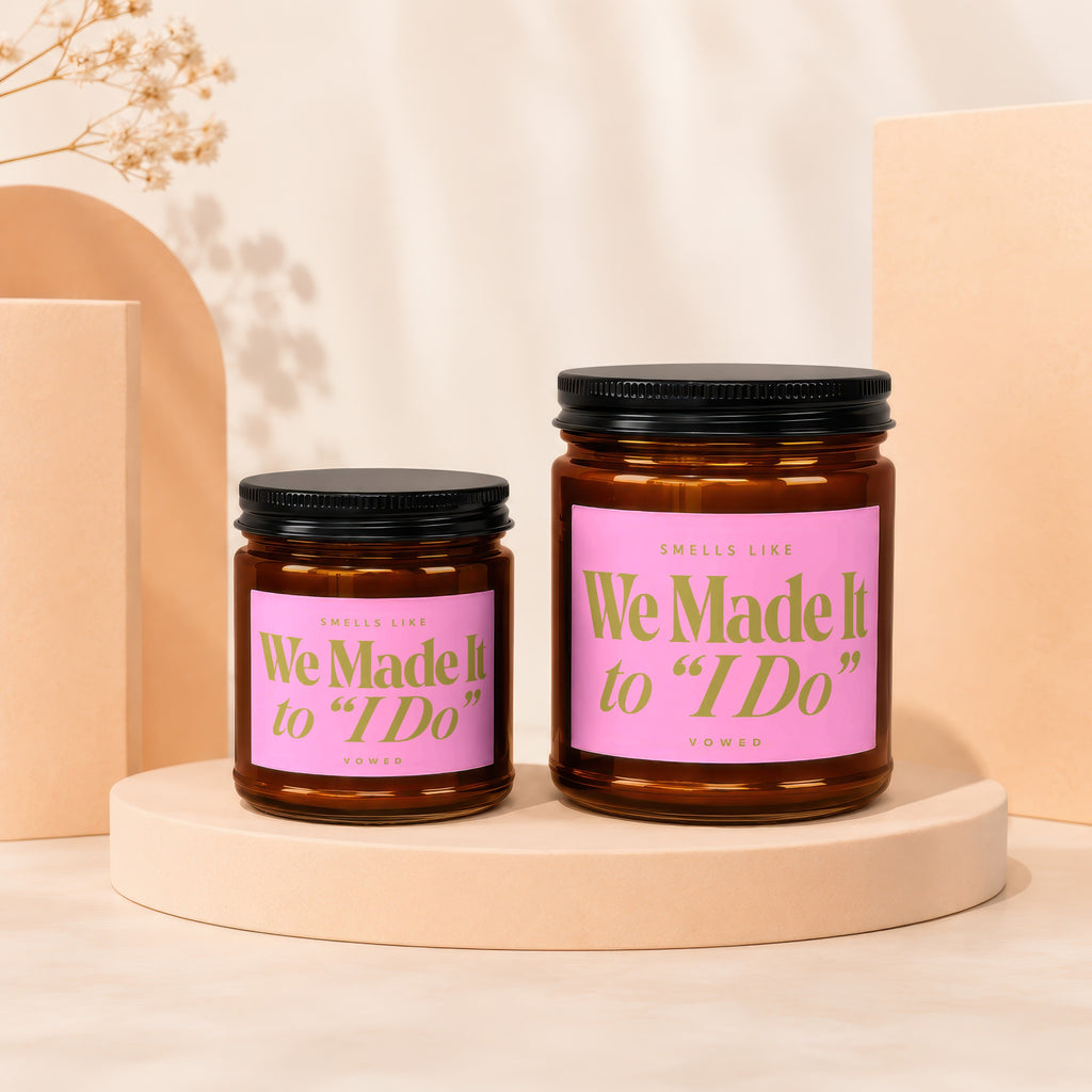 Two amber glass candles with pink labels reading "We Made It to 'I Do'".