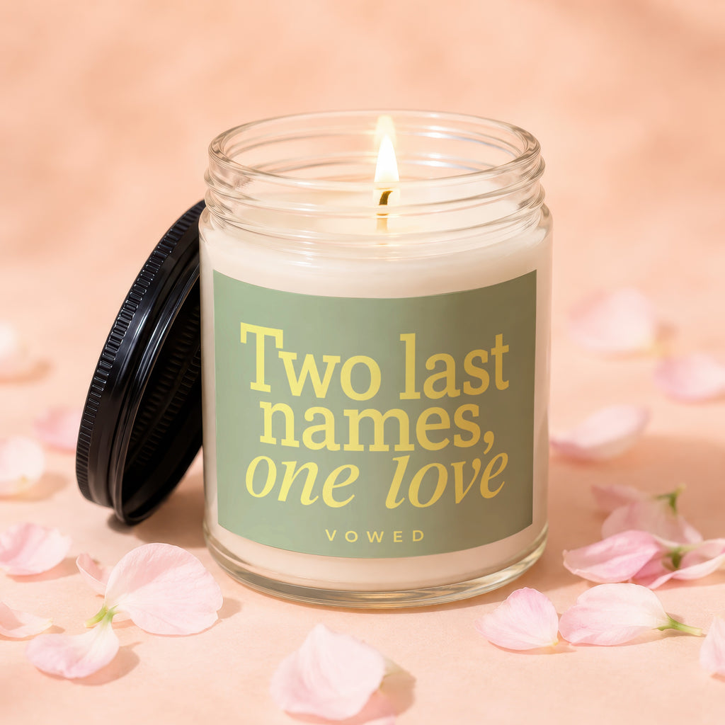 Jar candle with lit wick and "Two last names, one love" text on label.