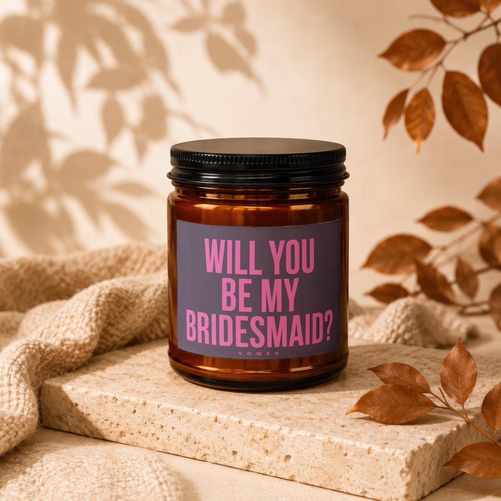 Candle with text "Will you be my bridesmaid?" on a stone block with autumn leaves.