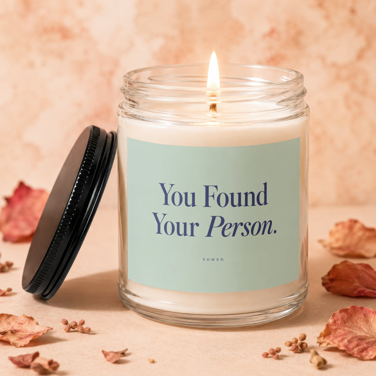 Candle with "You Found Your Person." text and lit wick surrounded by dried leaves.