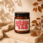 Amber candle with "SHE SAID YES" in pink retro font on label.