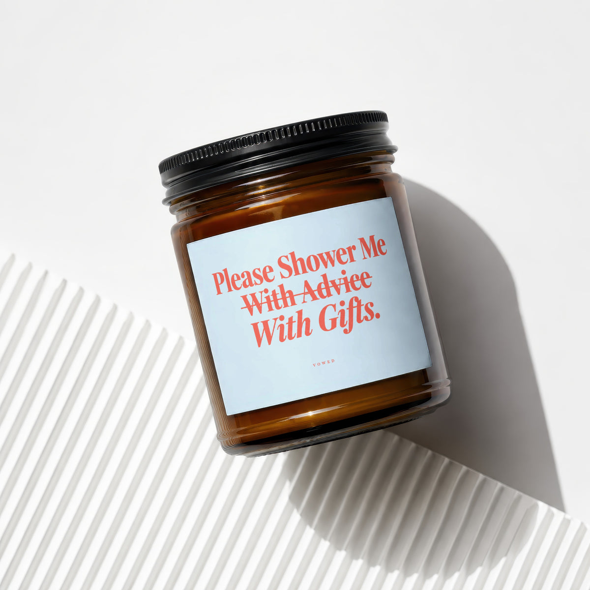 Amber glass candle with black lid and a light blue label reading "Please Shower Me With Advice With Gifts."