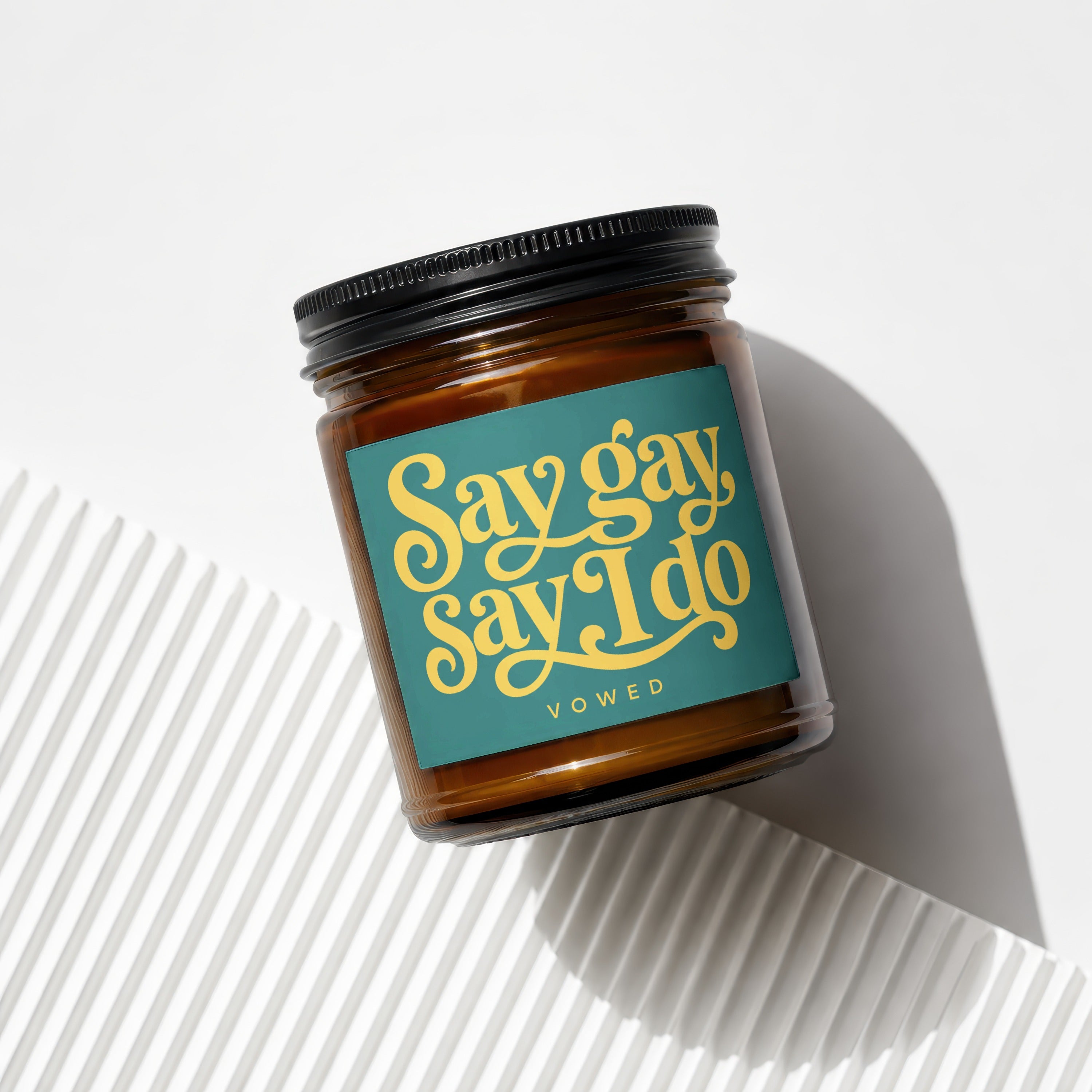 Amber glass candle with teal label that reads "Say gay, Say I do."