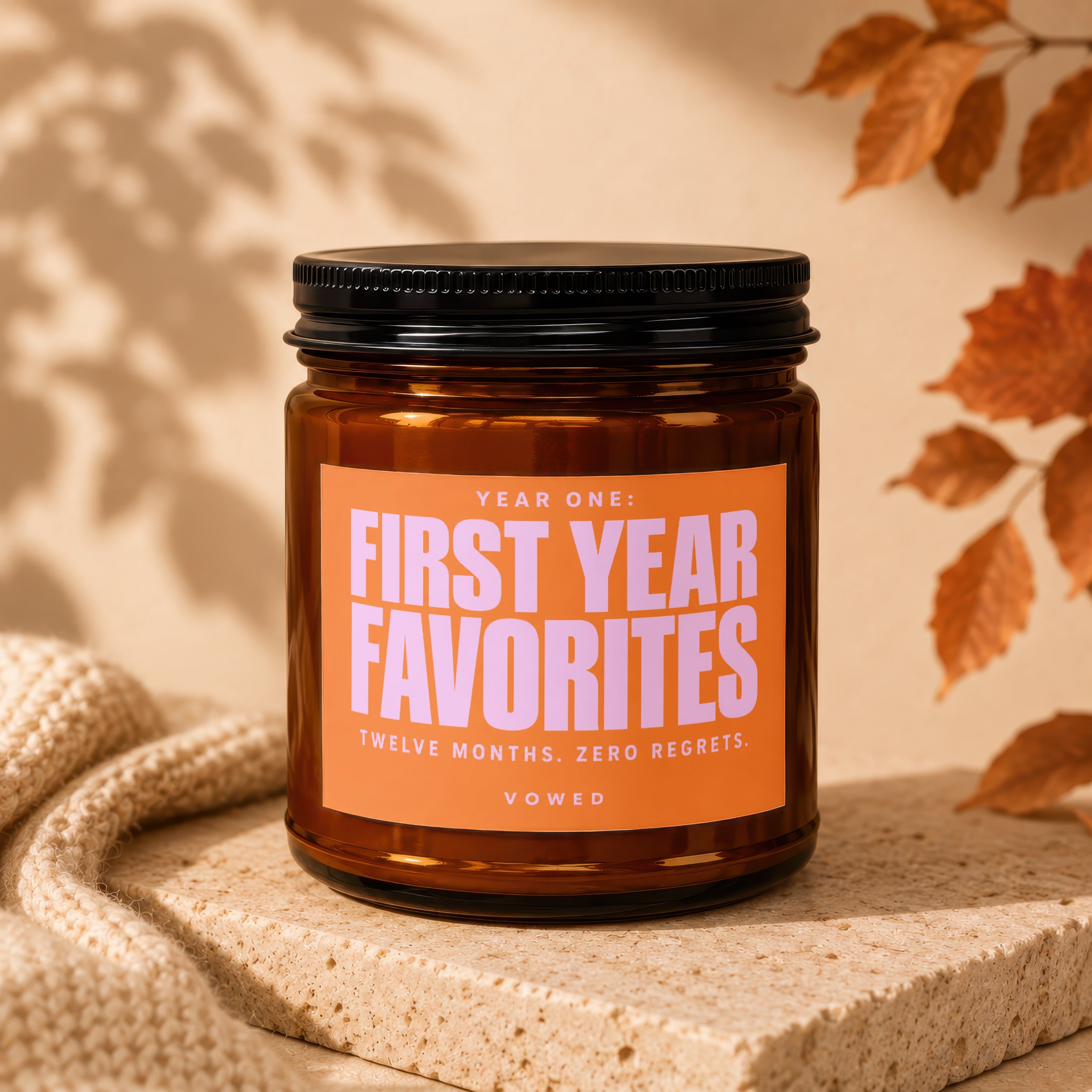 Amber jar candle with orange label reading "YEAR ONE: FIRST YEAR FAVORITES", "TWELVE MONTHS. ZERO REGRETS.", "VOWED".