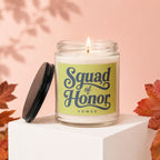 Glass candle with lit wick and "Squad of Honor VOWED" text on label.