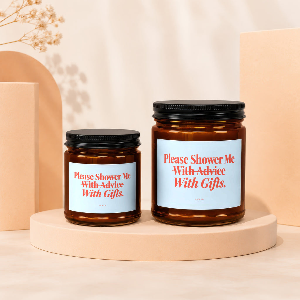 Two amber glass candles with black lids and light blue labels reading "Please Shower Me With Advice With Gifts."