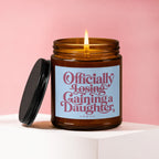 Amber candle with lit wick and black lid, reads "Officially Losing, Gaining a Daughter".