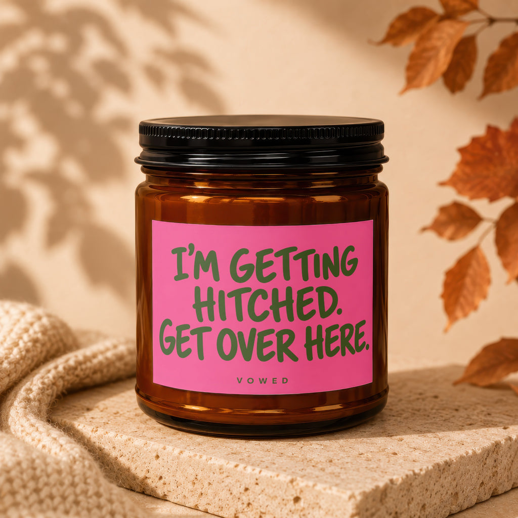 Amber glass candle with pink label reading "I'M GETTING HITCHED. GET OVER HERE."