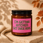 Amber glass candle with pink label reading "I'M GETTING HITCHED. GET OVER HERE."