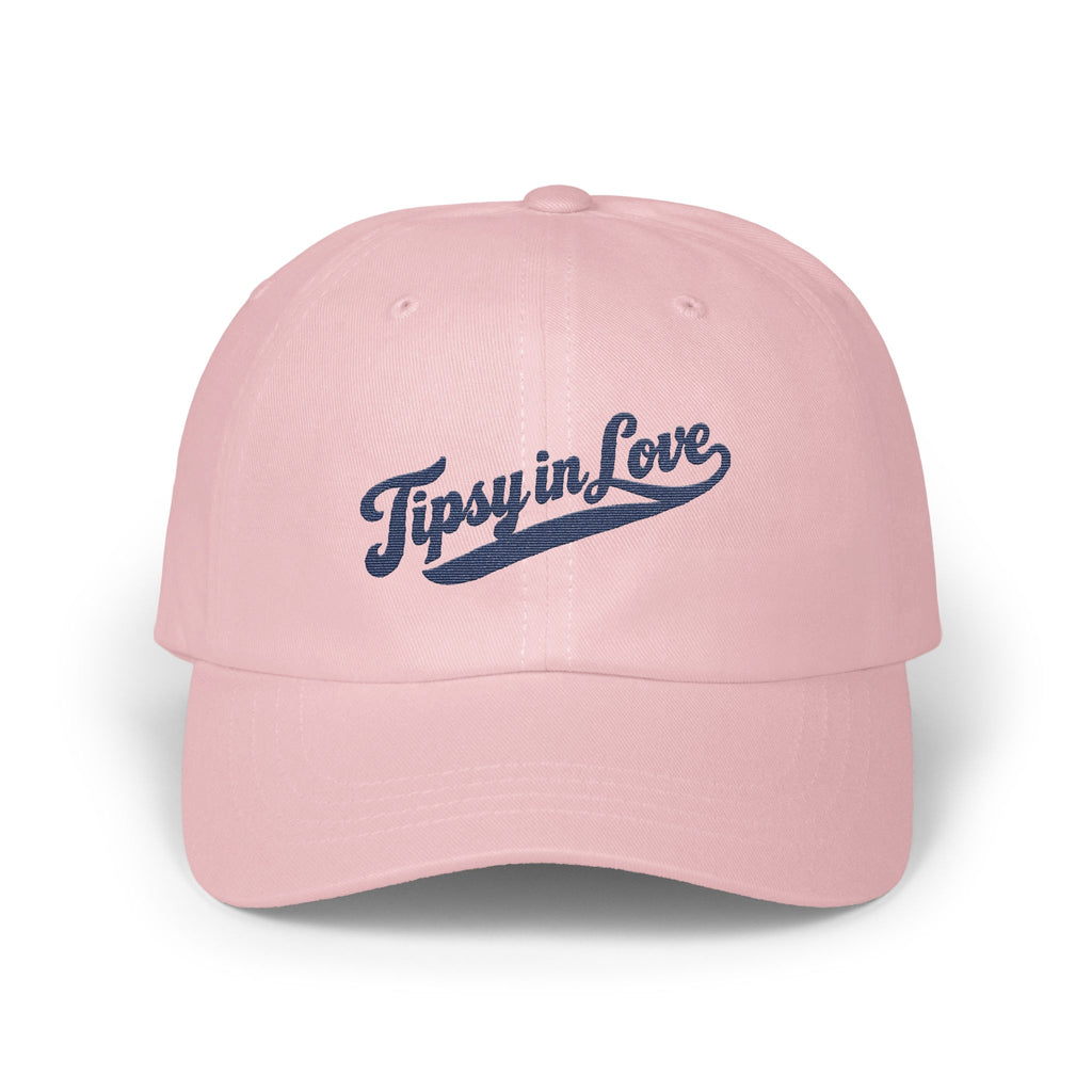 Light pink dad hat with the text Tipsy in Love embroidered in navy blue cursive.