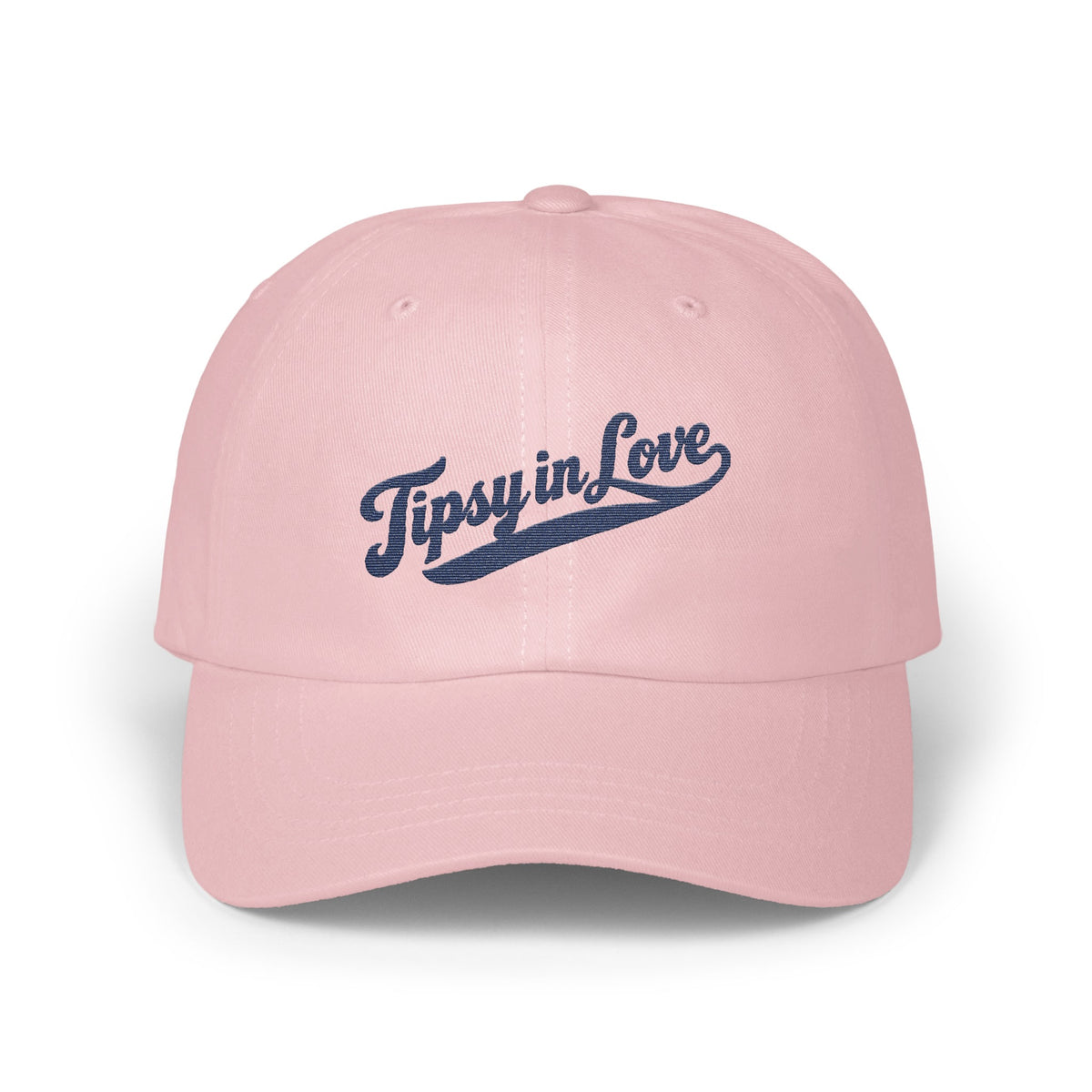 Light pink dad hat with the text Tipsy in Love embroidered in navy blue cursive.