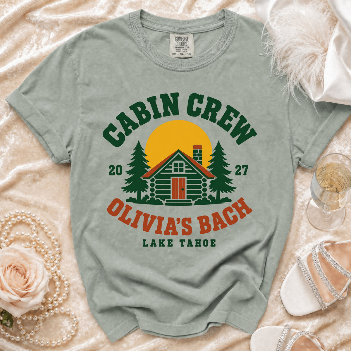 Sage green t-shirt featuring a retro cabin illustration with text that reads Cabin Crew Olivia's Bach Lake Tahoe.