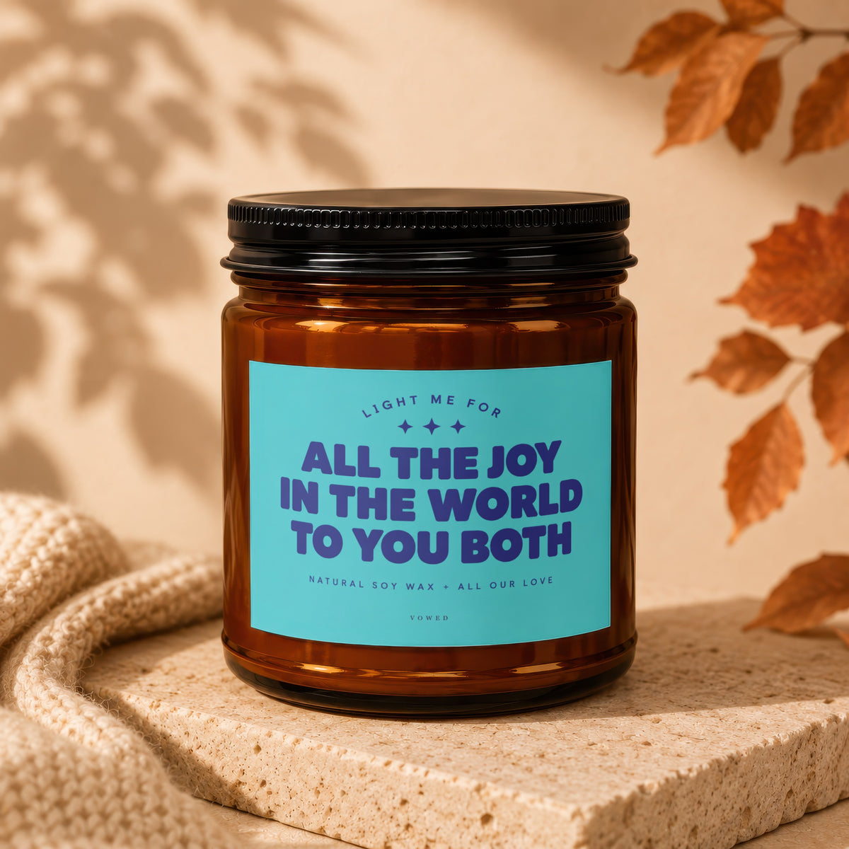 Amber jar candle with teal label reading "All the Joy in the World to You Both."