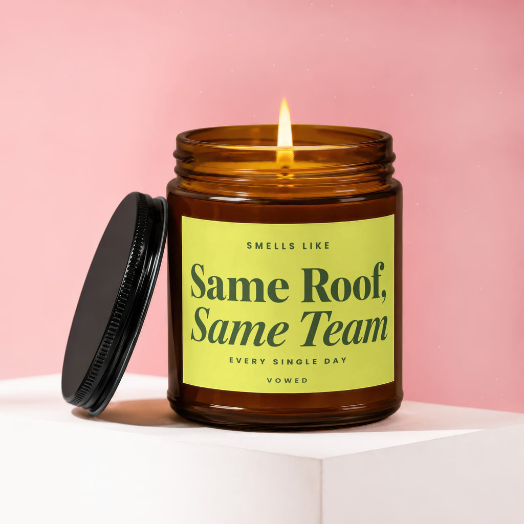 Lit amber glass candle with "Same Roof, Same Team" text on lime green label.